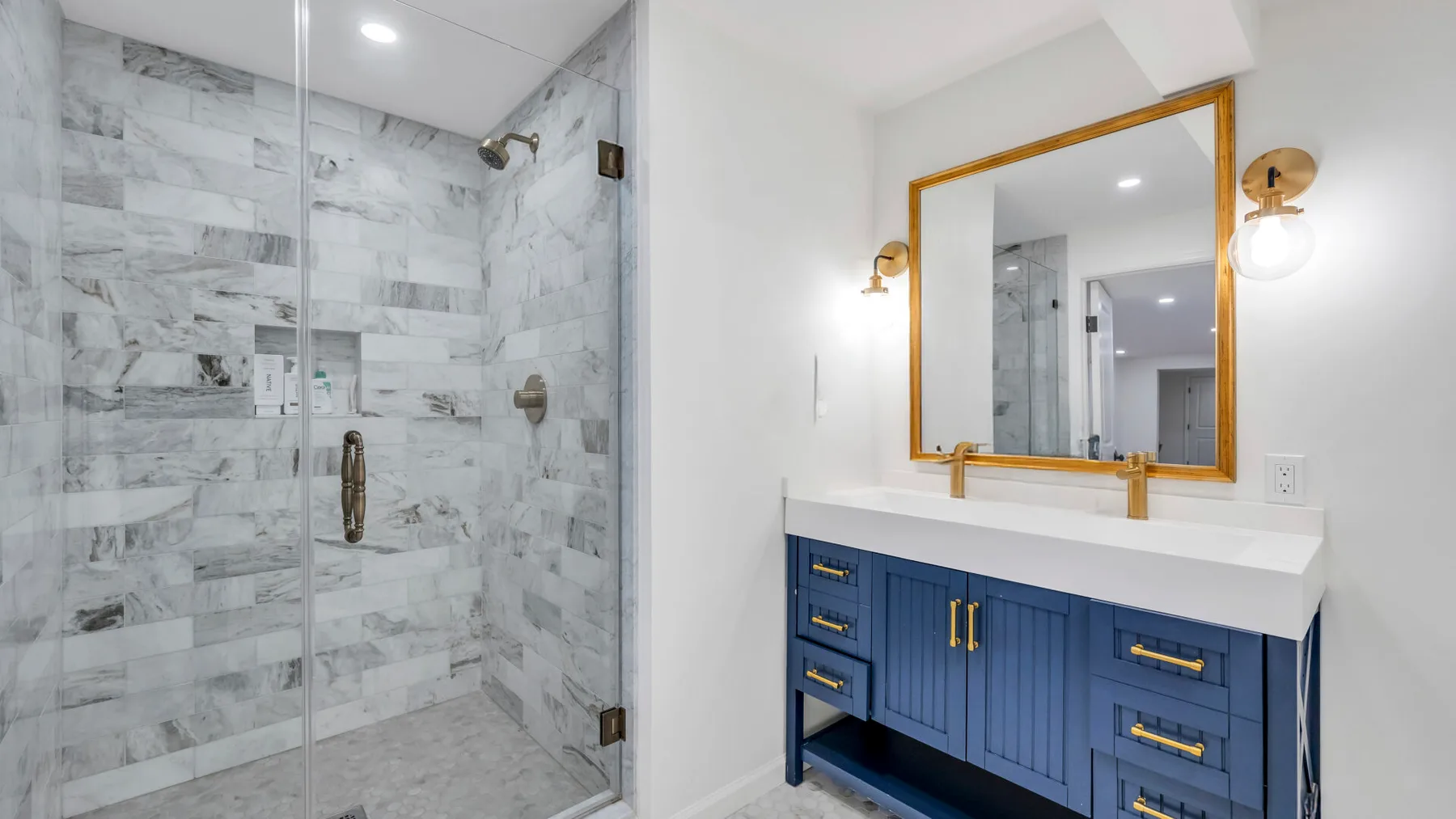 Un baño con una ducha de vidrio y un mueble azul bajo un espejo grande.