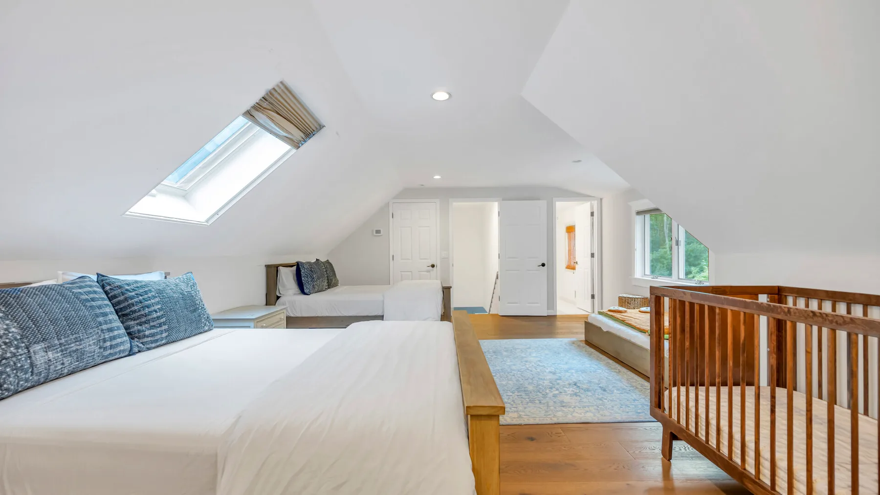 Un dormitorio abuhardillado luminoso con una cama grande, una claraboya y una barandilla de madera.