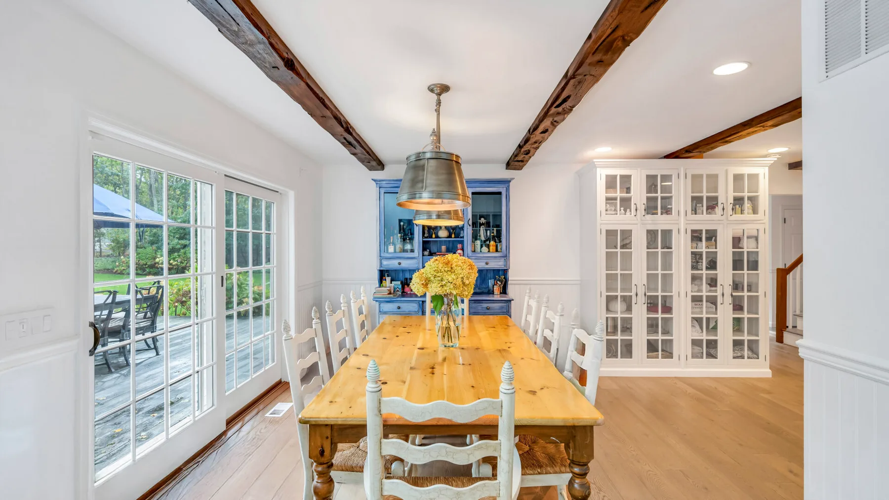 Un comedor con una larga mesa de madera y sillas blancas junto a grandes ventanas.