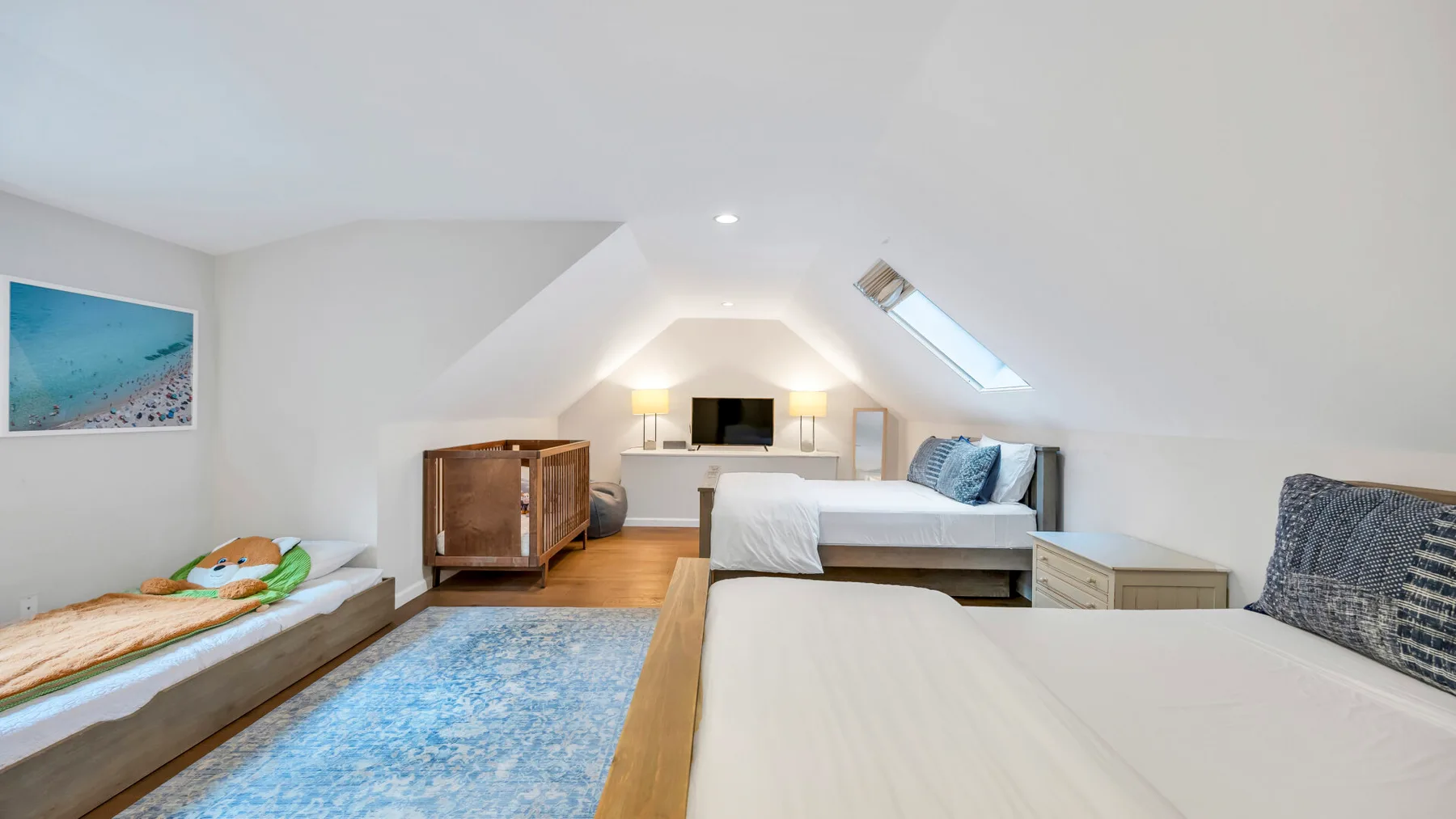 Un dormitorio abuhardillado luminoso con camas, una claraboya y una alfombra azul.