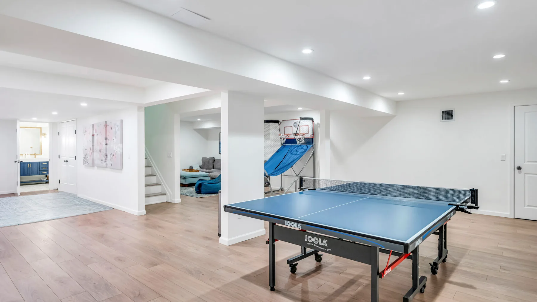 Una sala de recreación en un sótano con una mesa de ping-pong azul y una canasta de baloncesto.