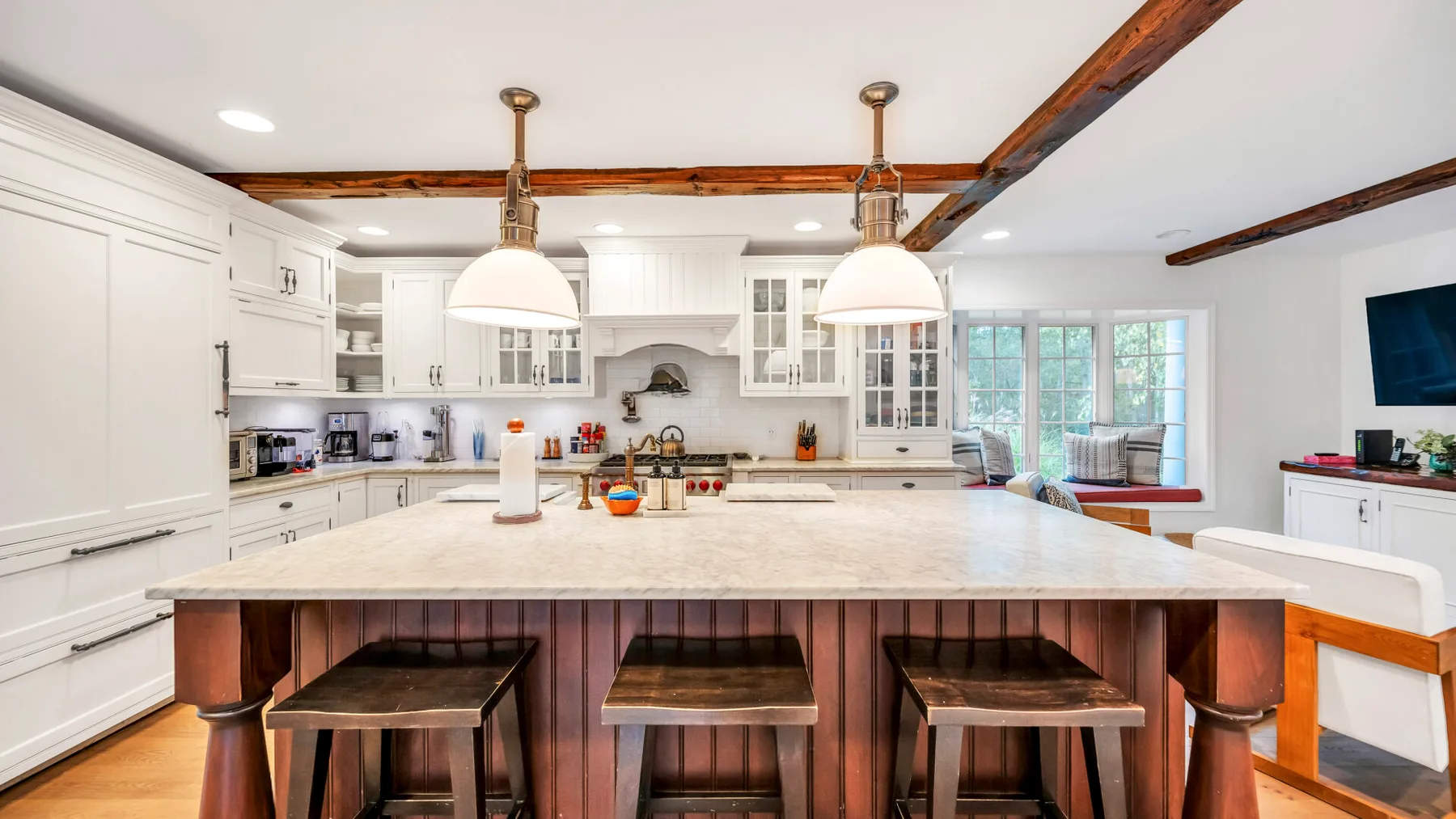 Una cocina luminosa con una isla grande, lámparas colgantes y gabinetes blancos.