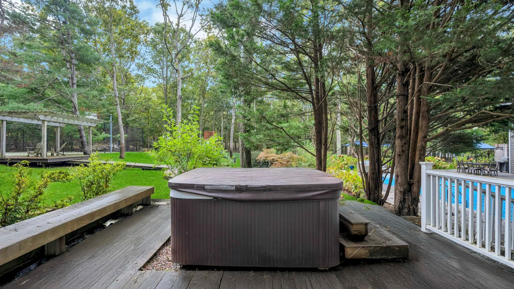 Una terraza de madera con una bañera de hidromasaje redonda está entre árboles.