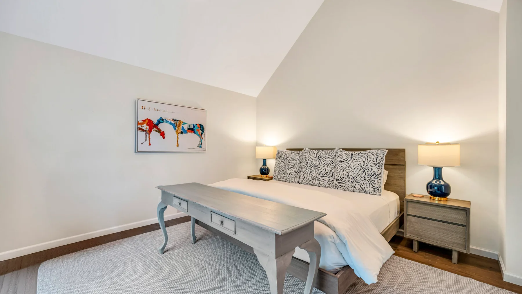 Un dormitorio con una cama, mesitas de noche a juego y una mesa a los pies de la cama.