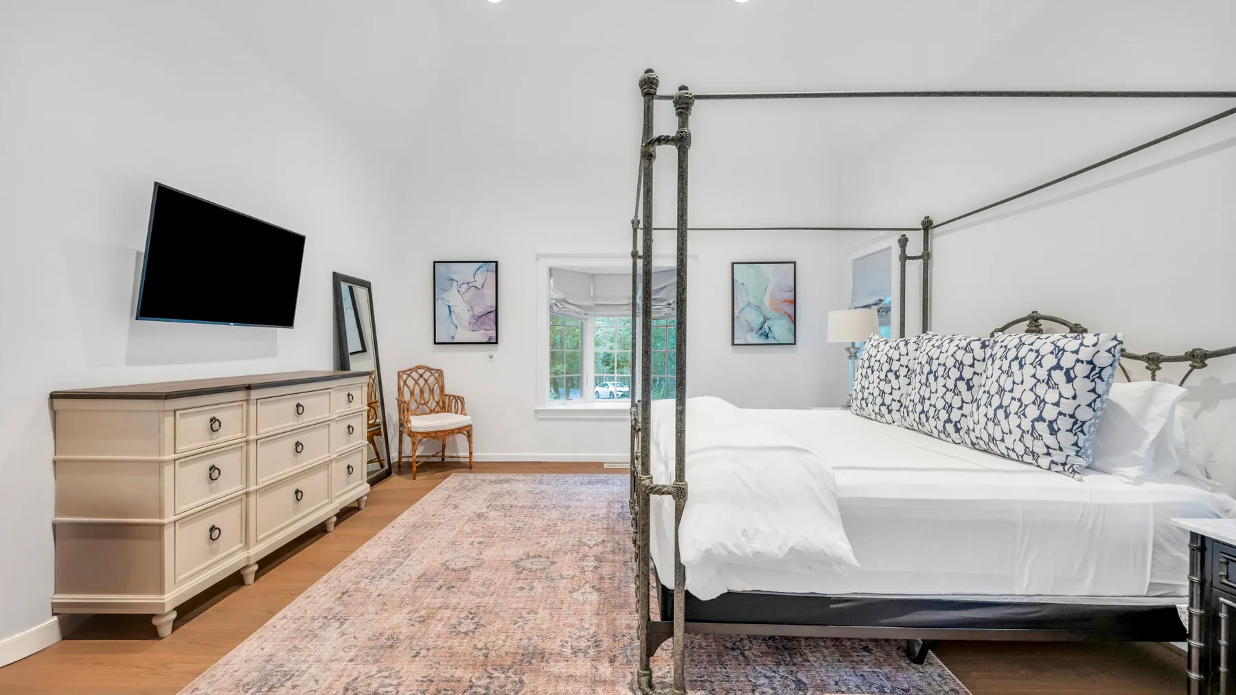 Un dormitorio luminoso con una cama con dosel y una cómoda bajo un televisor en la pared.