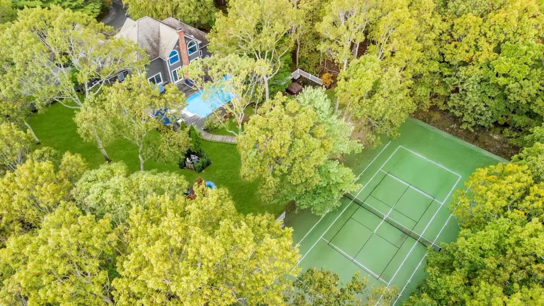 Una vista aérea muestra una cancha de tenis y una piscina entre árboles.