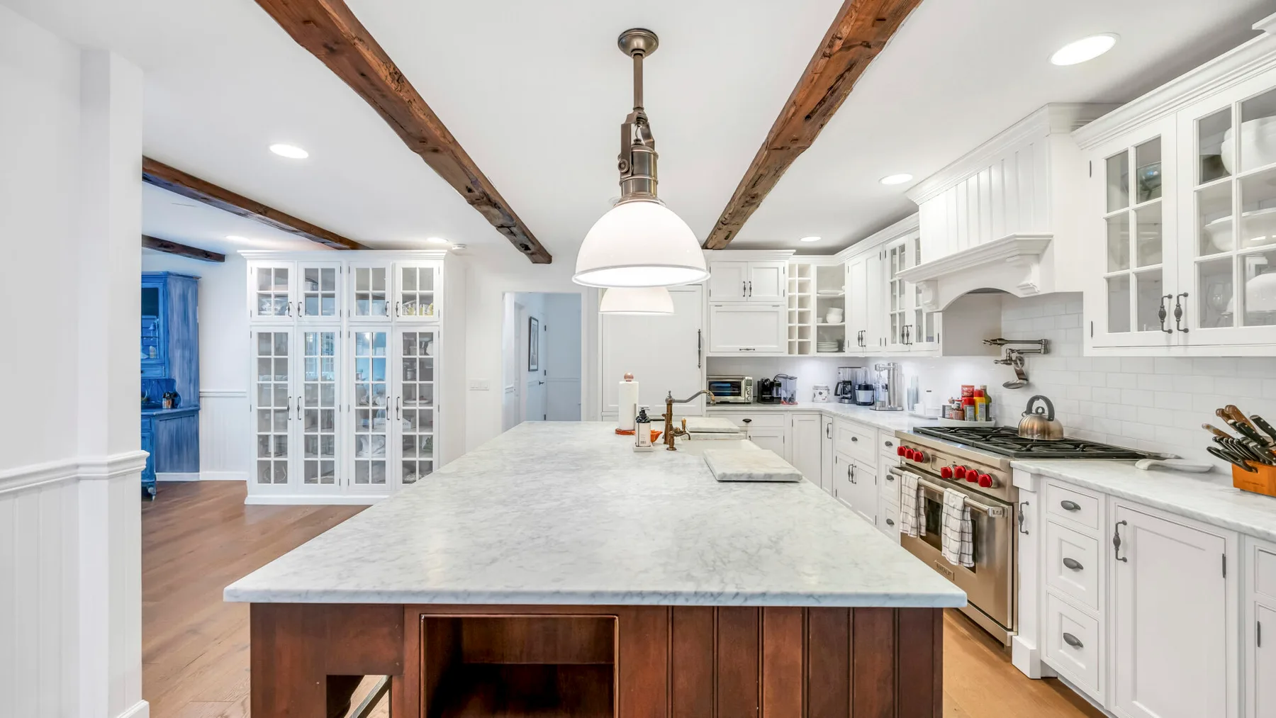 Una cocina blanca y luminosa con una isla grande y armarios con puertas de vidrio.
