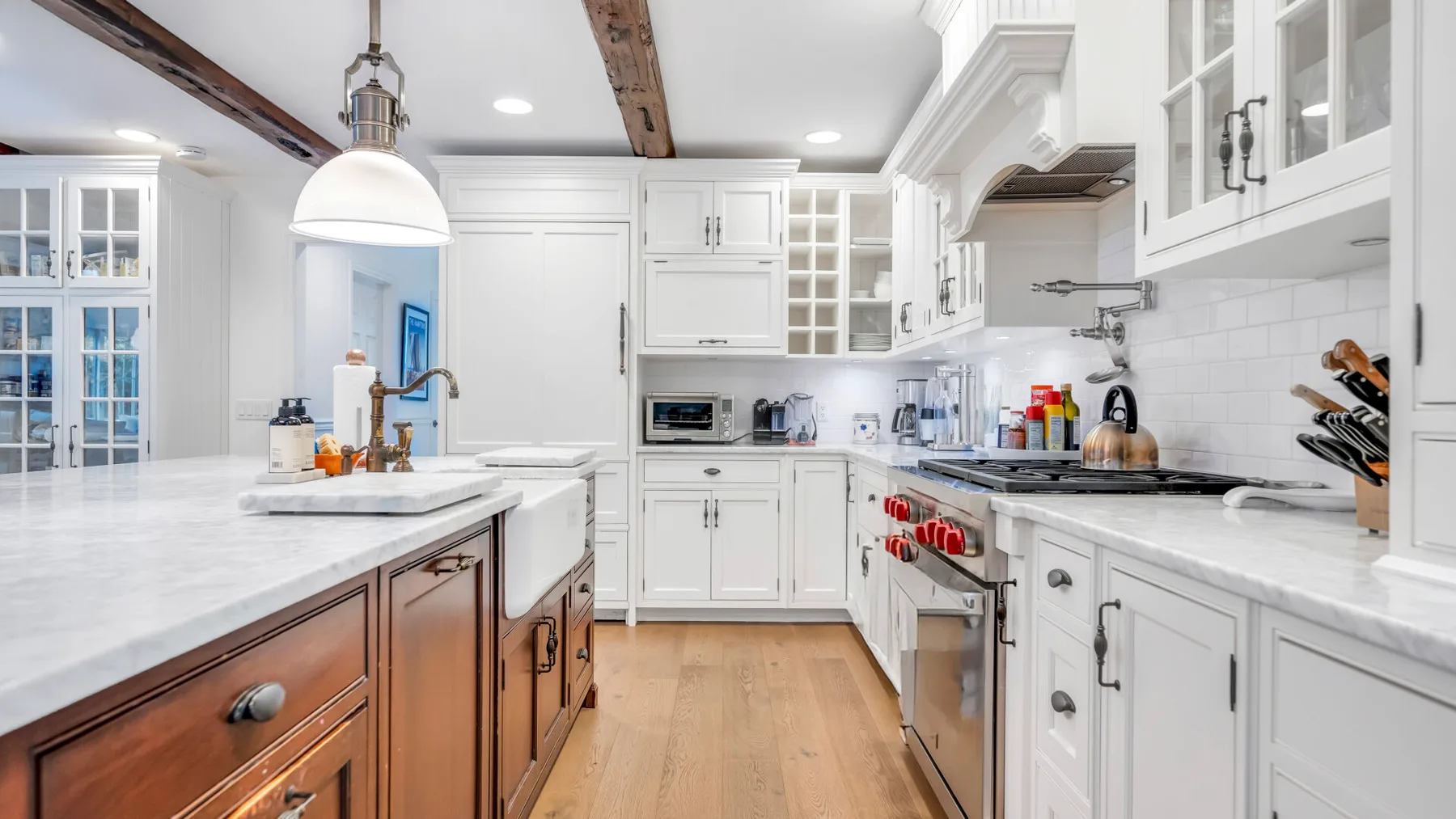 Una cocina luminosa con gabinetes blancos, una isla central y piso de madera.