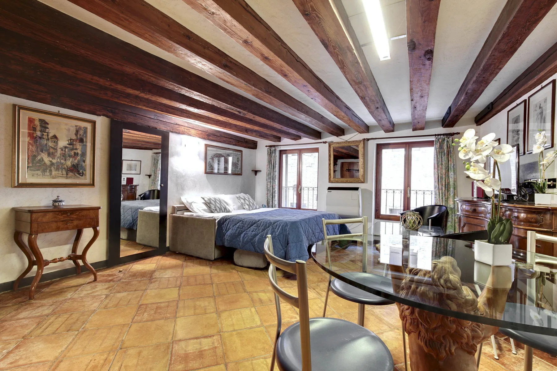 Un dormitorio con una cama, vigas expuestas en el techo y una mesa de cristal.