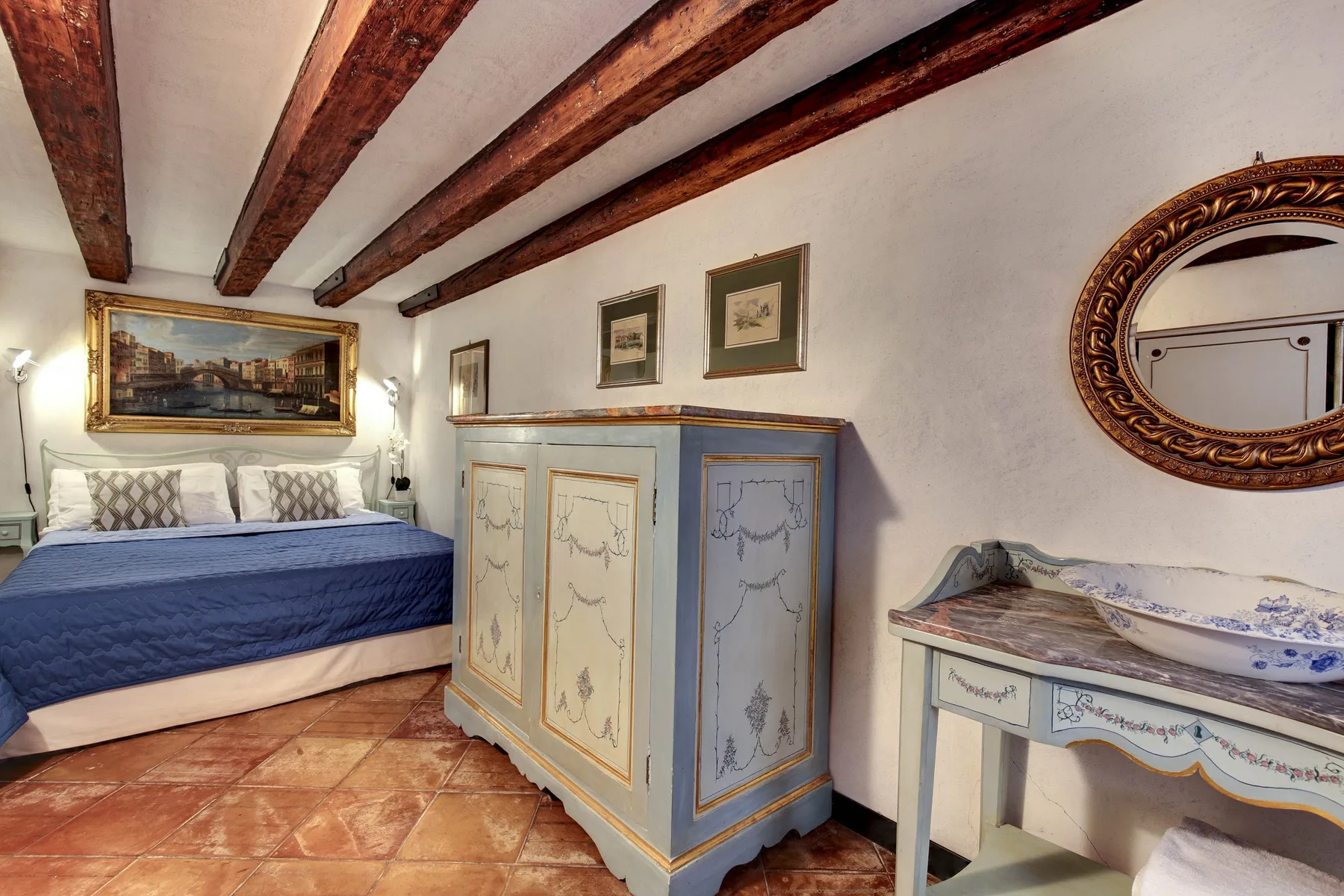 Un dormitorio con una cama cubierta de azul, un armario pintado y vigas de madera a la vista.