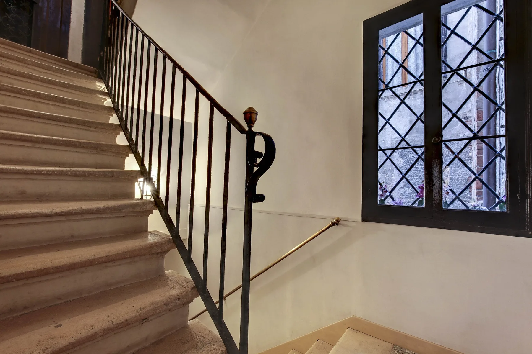 Una escalera interior con una barandilla de metal oscuro junto a una ventana.