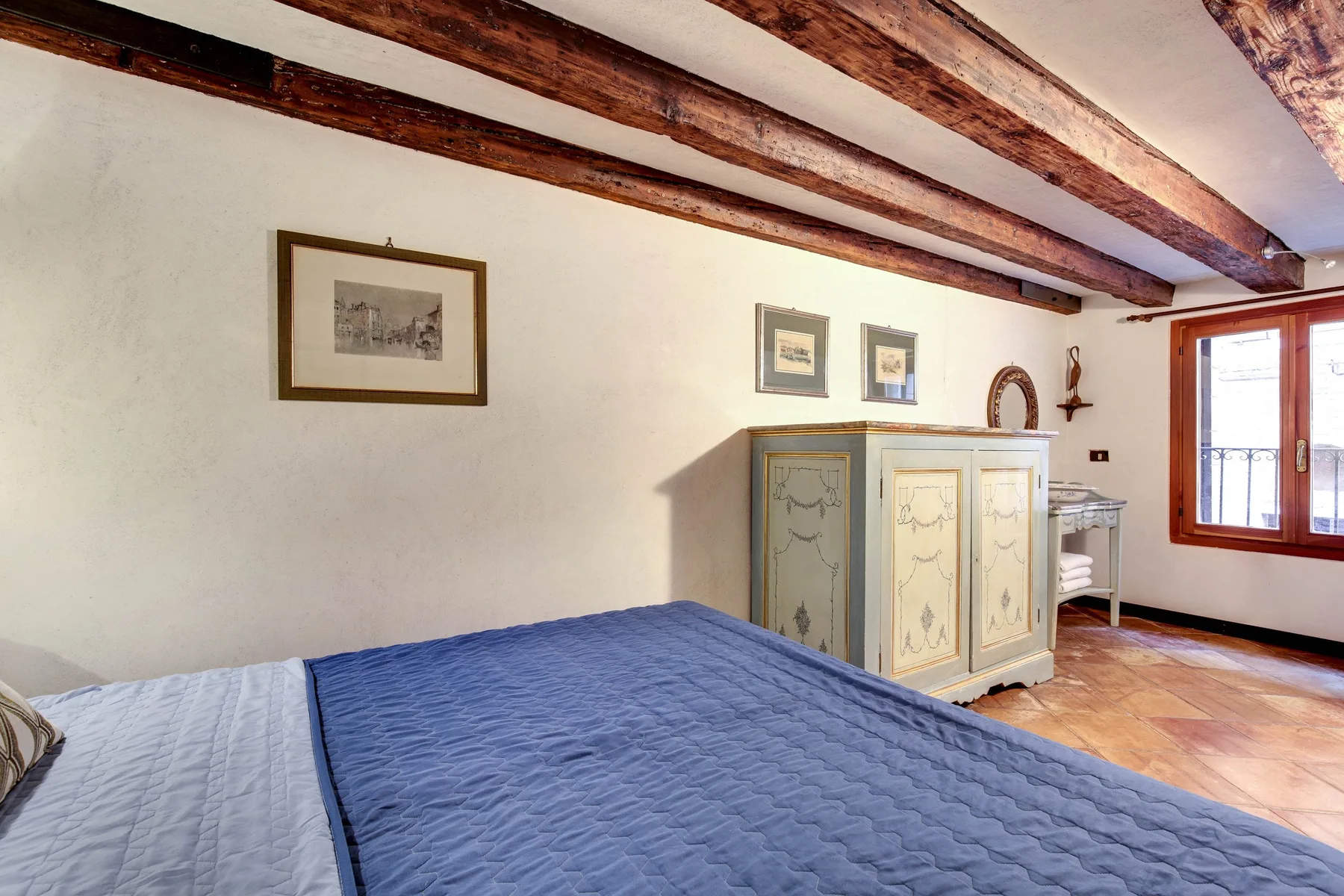 Un dormitorio con una colcha azul, vigas de madera en el techo y una ventana.