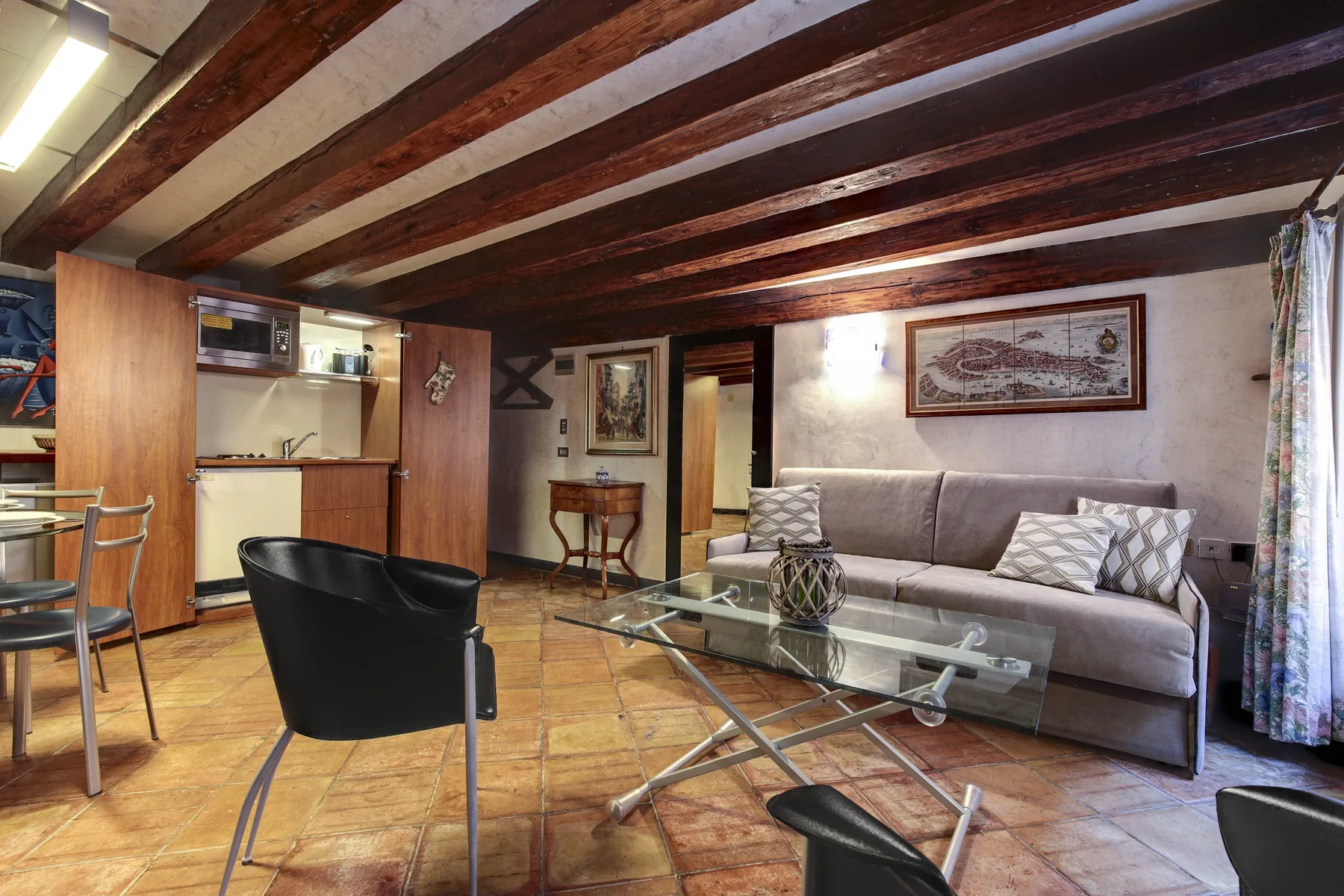 Una sala de estar con sofá, mesa de centro de vidrio y vigas de madera expuestas.