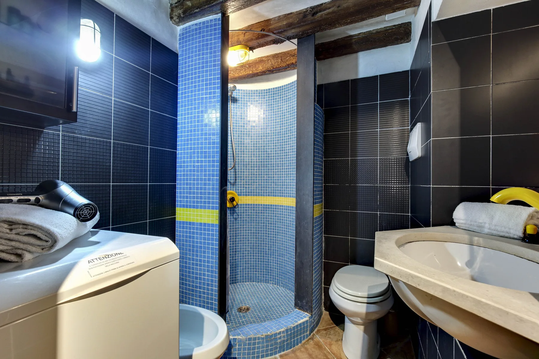 Un baño pequeño con azulejos, ducha curva, inodoro, lavabo y lavadora.