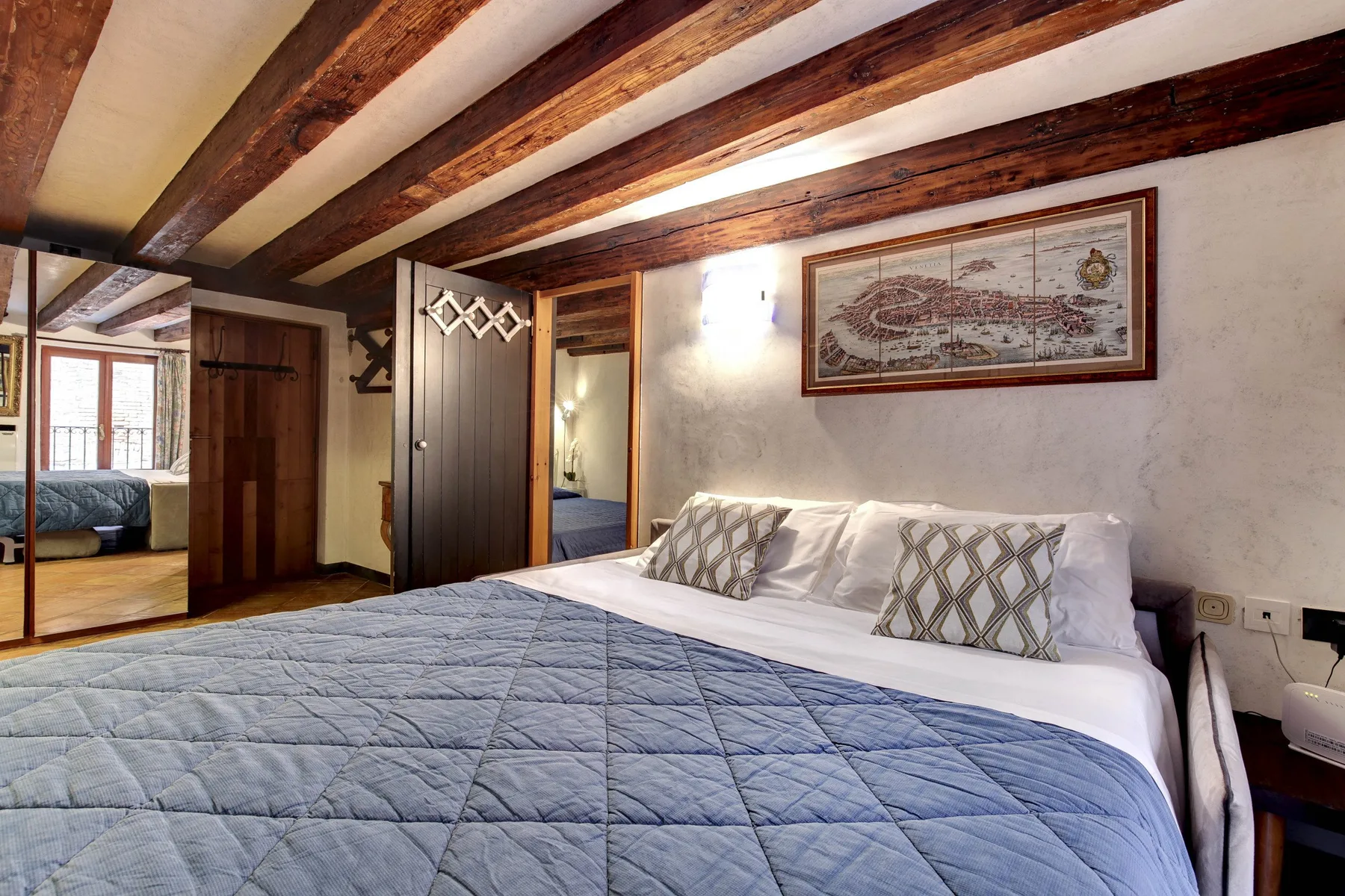 Un dormitorio con una cama grande, ropa de cama estampada y vigas de madera expuestas en el techo.