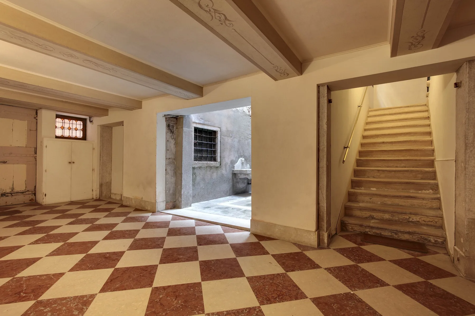 Un recibidor embaldosado con una puerta a un patio y escaleras junto a la pared.