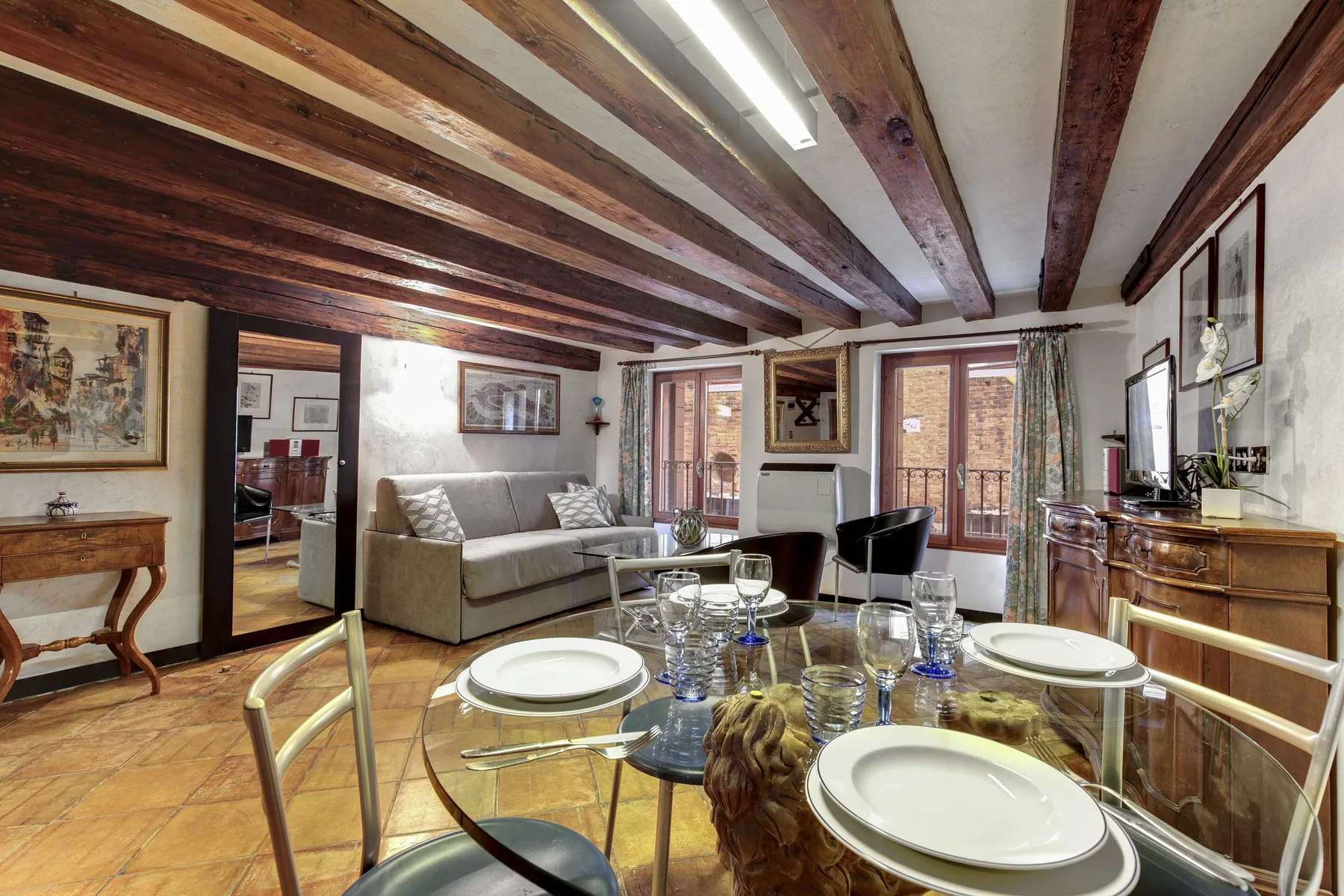Un comedor con una mesa de vidrio puesta y un sofá al fondo.