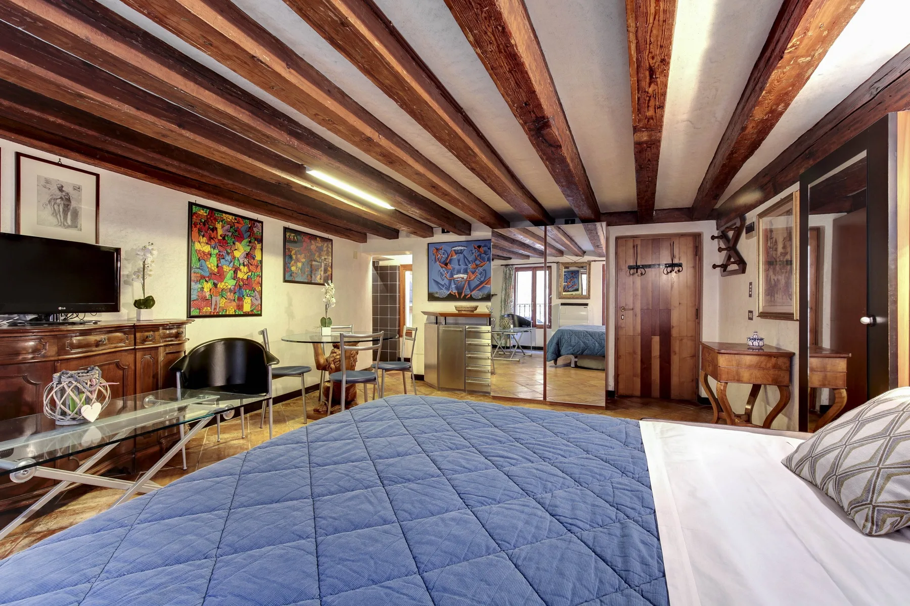 Un dormitorio con una cama cubierta de azul, vigas expuestas y asientos.
