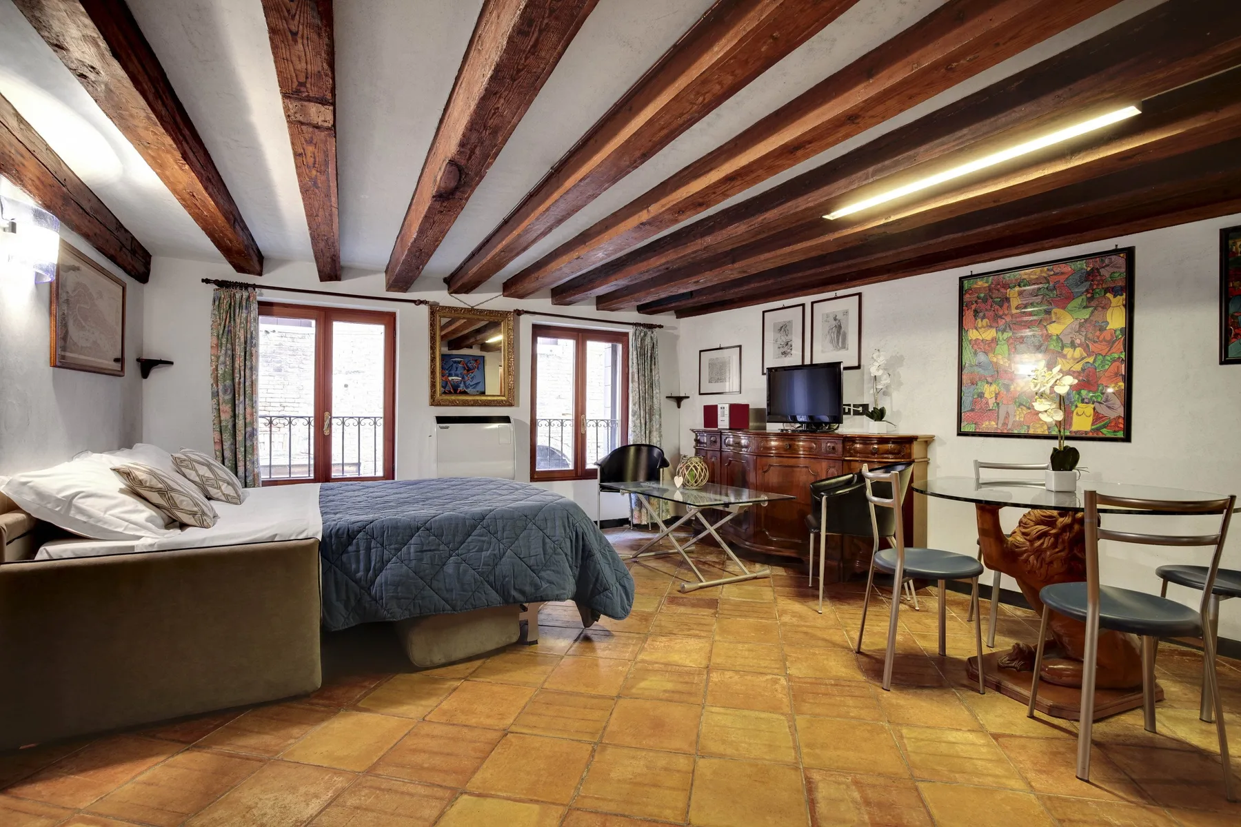 Dormitorio y zona de estar con una cama, una mesa de comedor y vigas expuestas.
