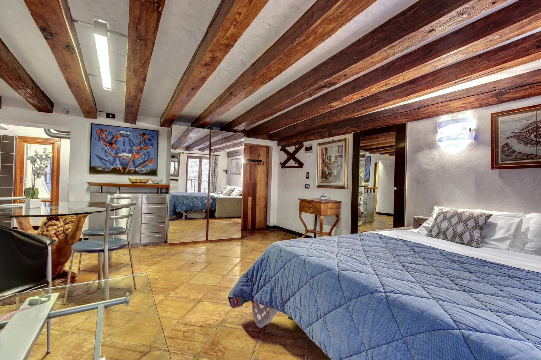 Un dormitorio con una cama cubierta de azul, vigas vistas y una pequeña zona de estar.