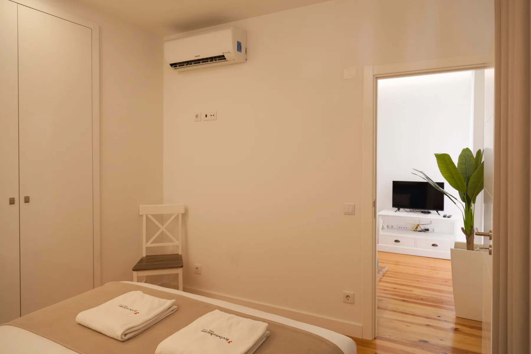 Un dormitorio con toallas dobladas sobre la cama y una puerta abierta a una sala de estar.