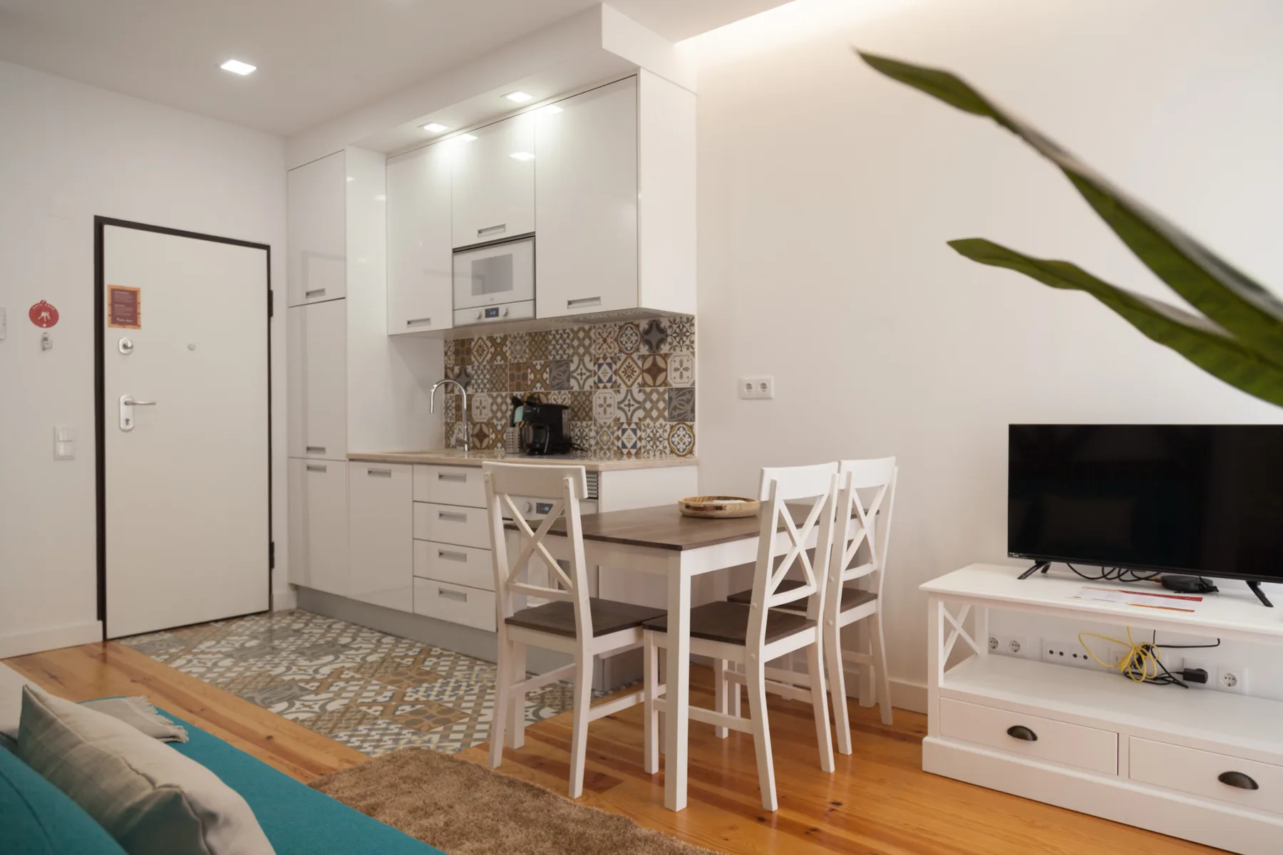 Una zona compacta de estar y comedor con cocina blanca y televisor.