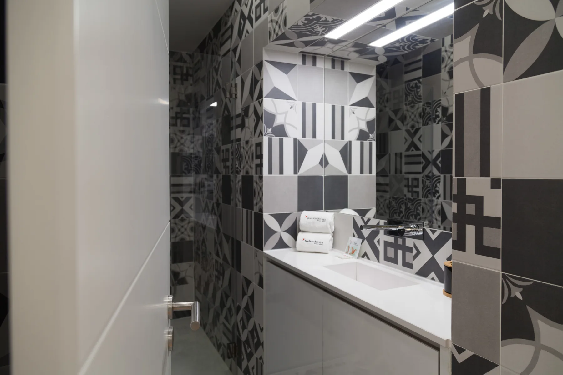 Un baño con un lavabo blanco y paredes de azulejos estampados en blanco y negro.