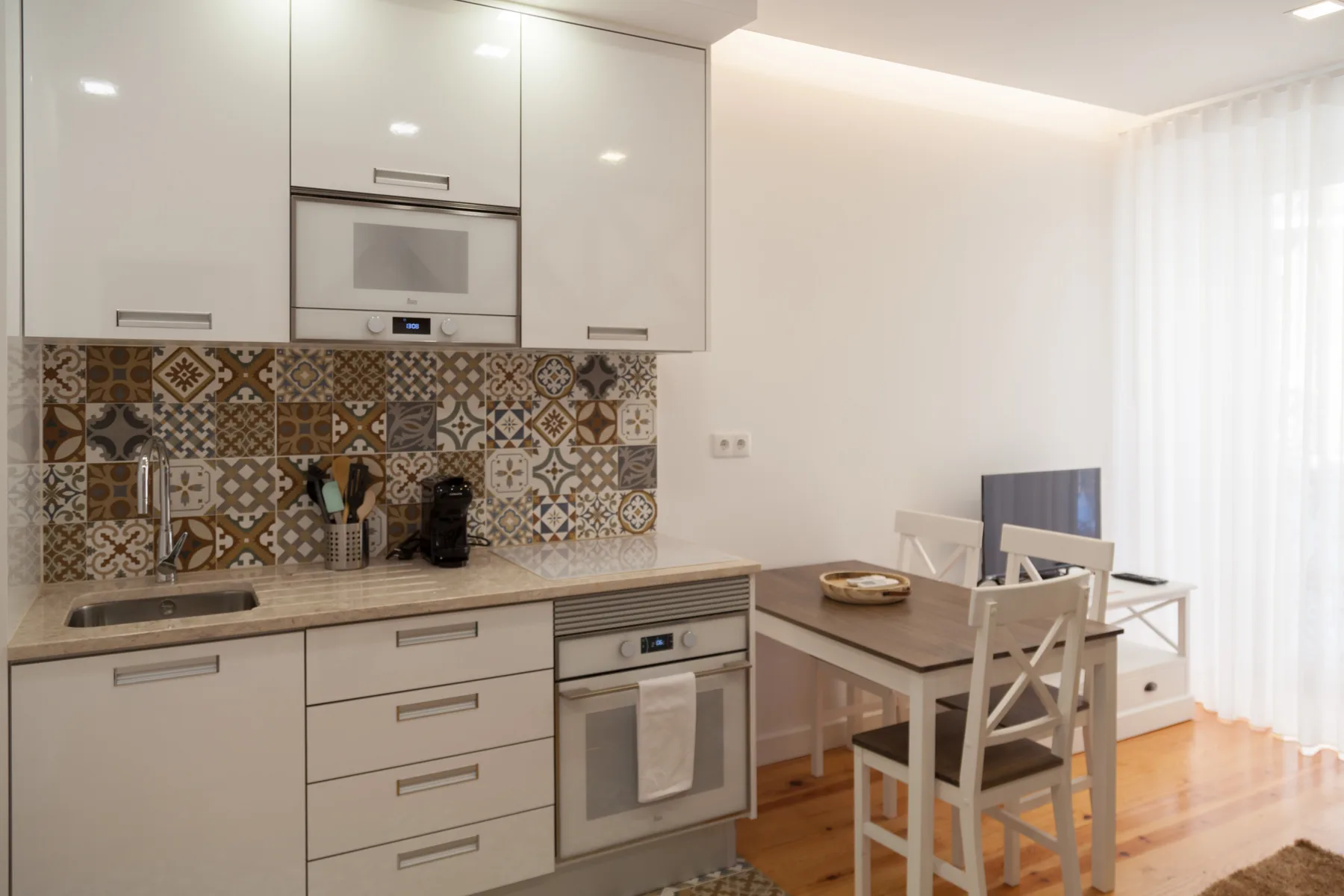 Una cocina y comedor luminosos con gabinetes blancos y un salpicadero estampado.