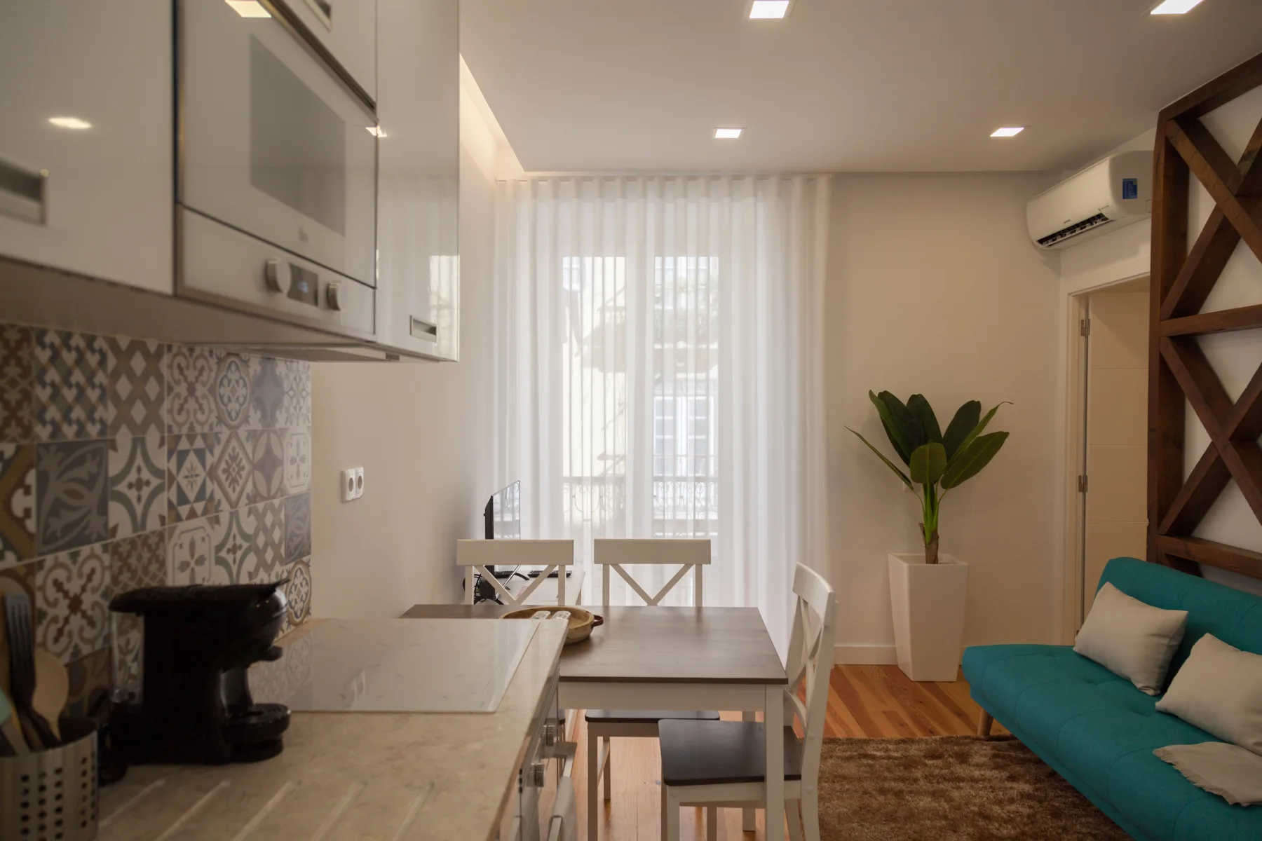 Una luminosa zona de comedor y estar con mesa, asientos y una planta en maceta.
