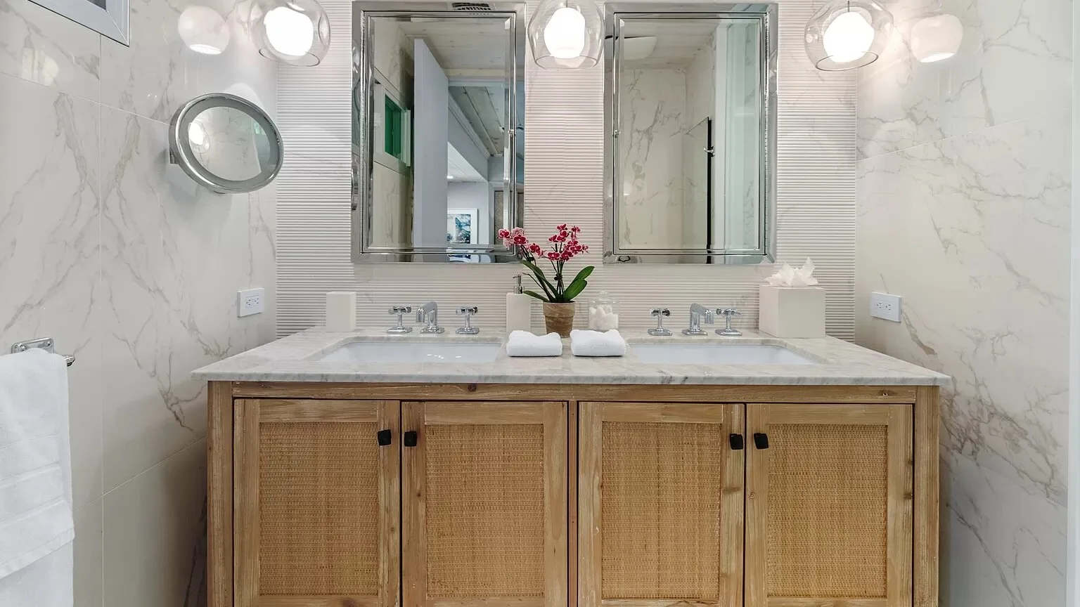 Un tocador de baño con un espejo amplio y flores sobre la encimera.