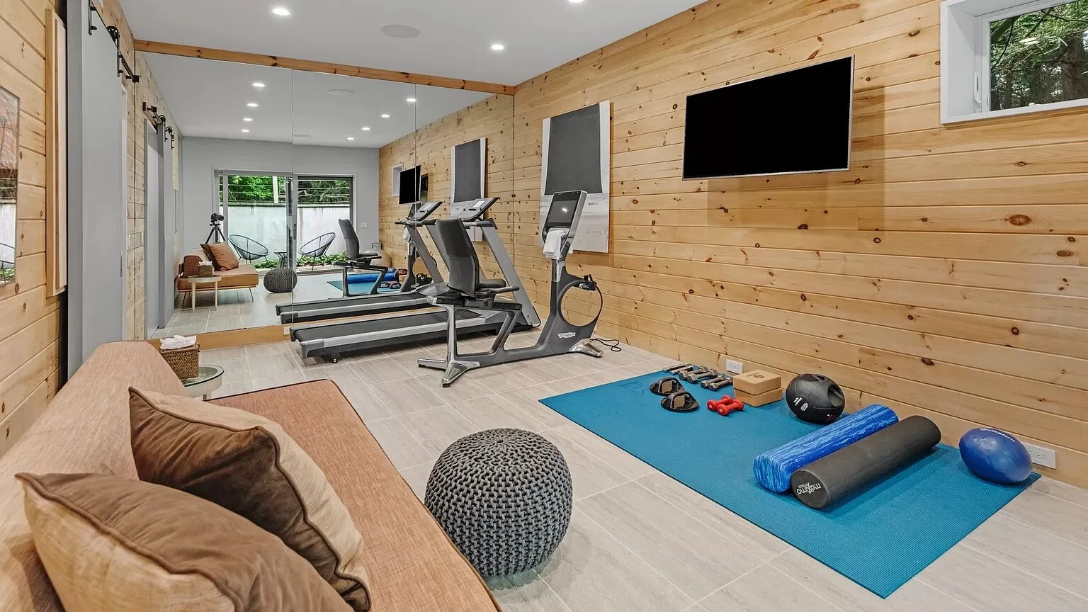 Un gimnasio en casa con equipo de ejercicio, una colchoneta azul y un televisor en la pared.