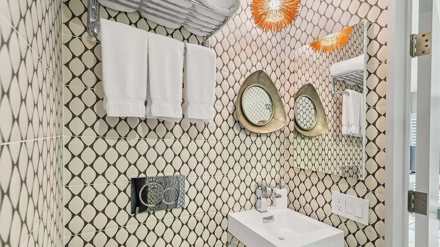Un baño de azulejos estampados con lavabo, espejo y toallas colgadas.