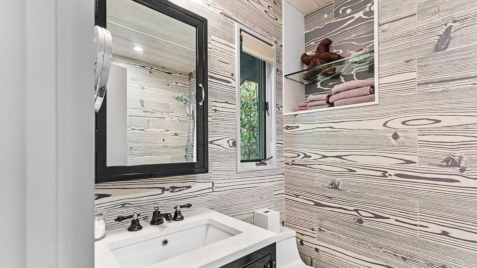 Un baño con un lavabo blanco debajo de un espejo con marco negro.