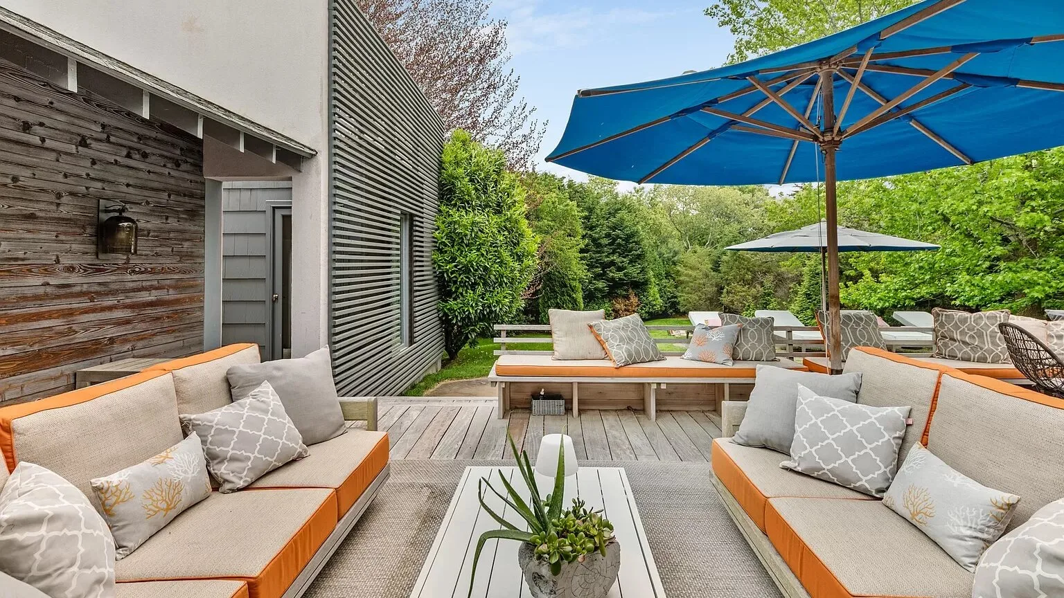 Una zona de estar en un patio exterior con bancos acolchados y una sombrilla azul.