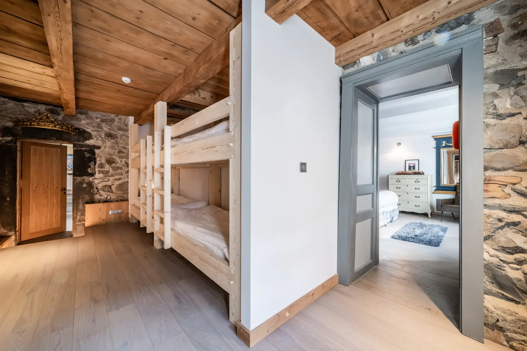 A bedroom with wooden bunk beds and an adjoining room visible through the doorway.
