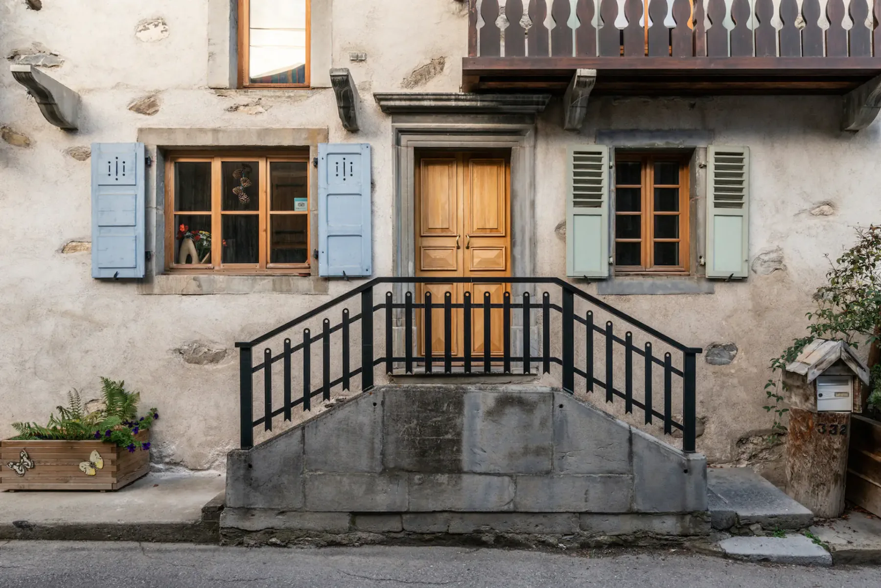 Stone chalet facade with a wooden entrance door, shuttered windows, and a front stairway.