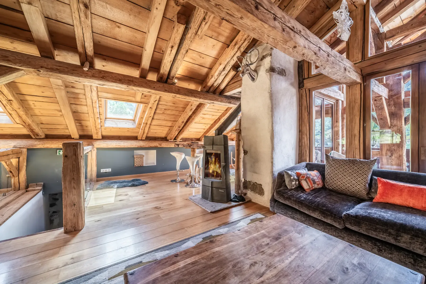 A rustic living area with exposed wooden beams and seating beside the windows.