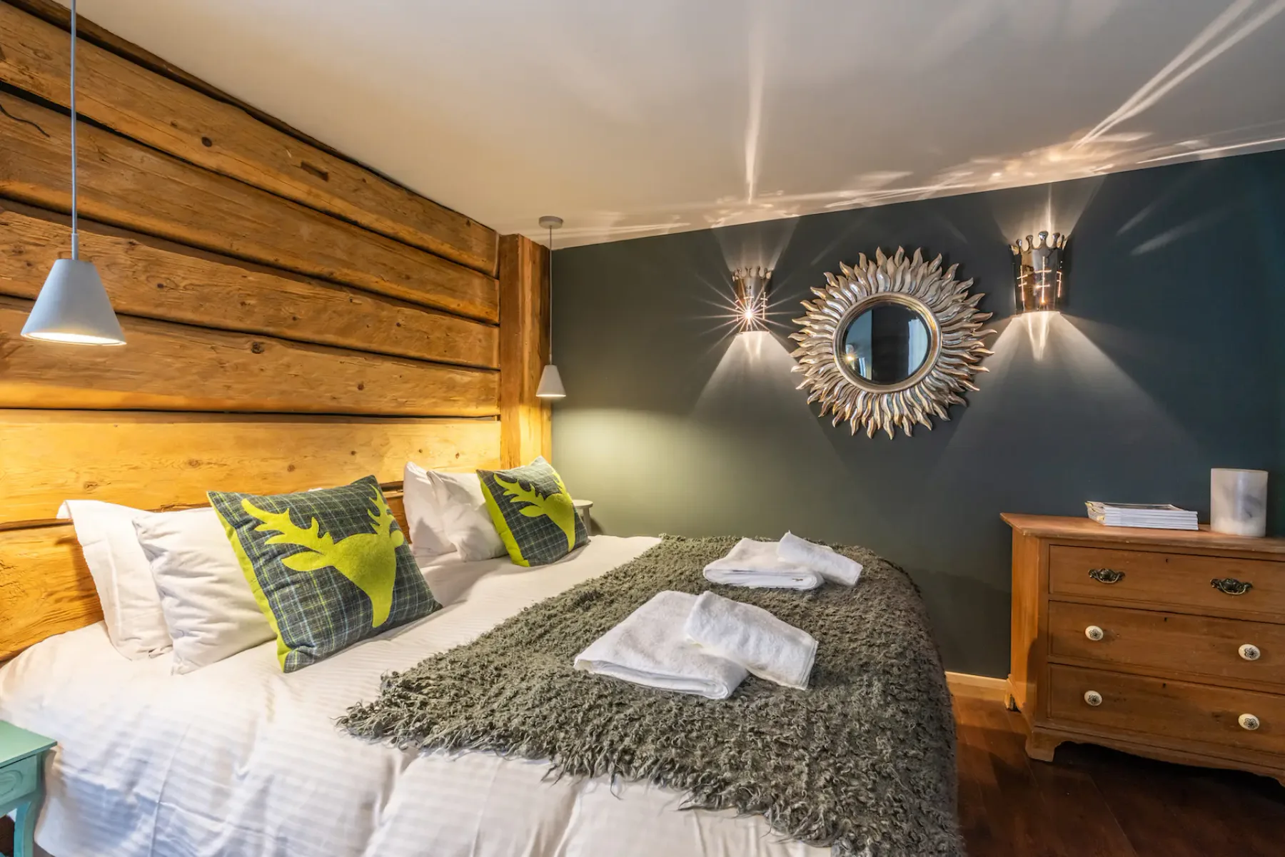 A bedroom with a double bed, decorative cushions, and a wooden chest of drawers.