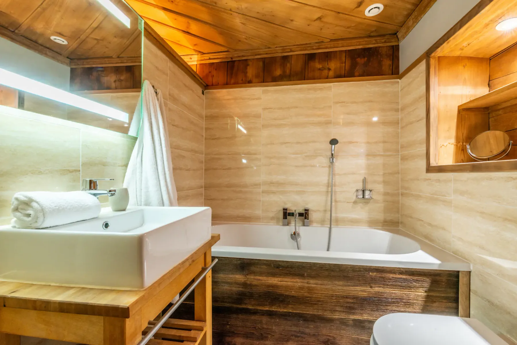 A bathroom with a bathtub, handheld shower, and wooden vanity.