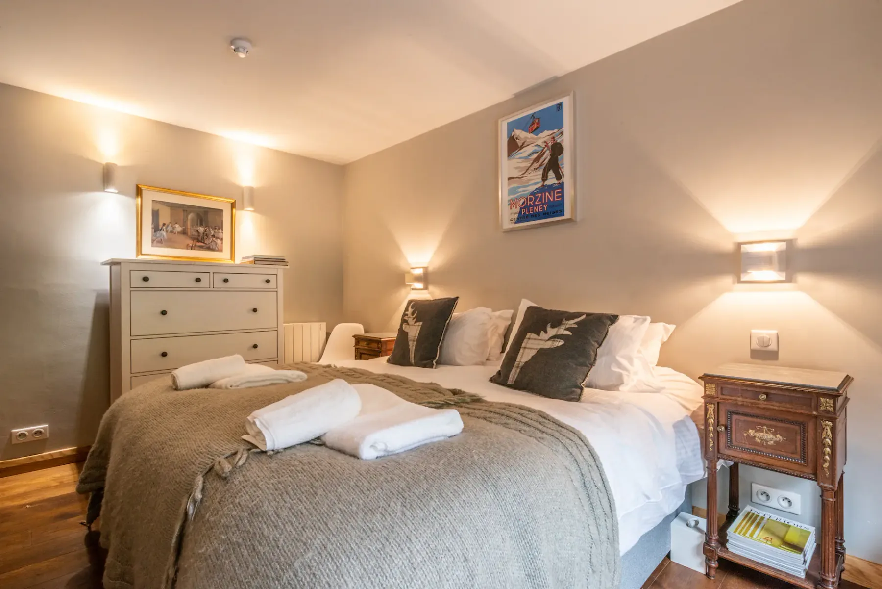 A bedroom with a made bed, folded towels, and bedside lighting.