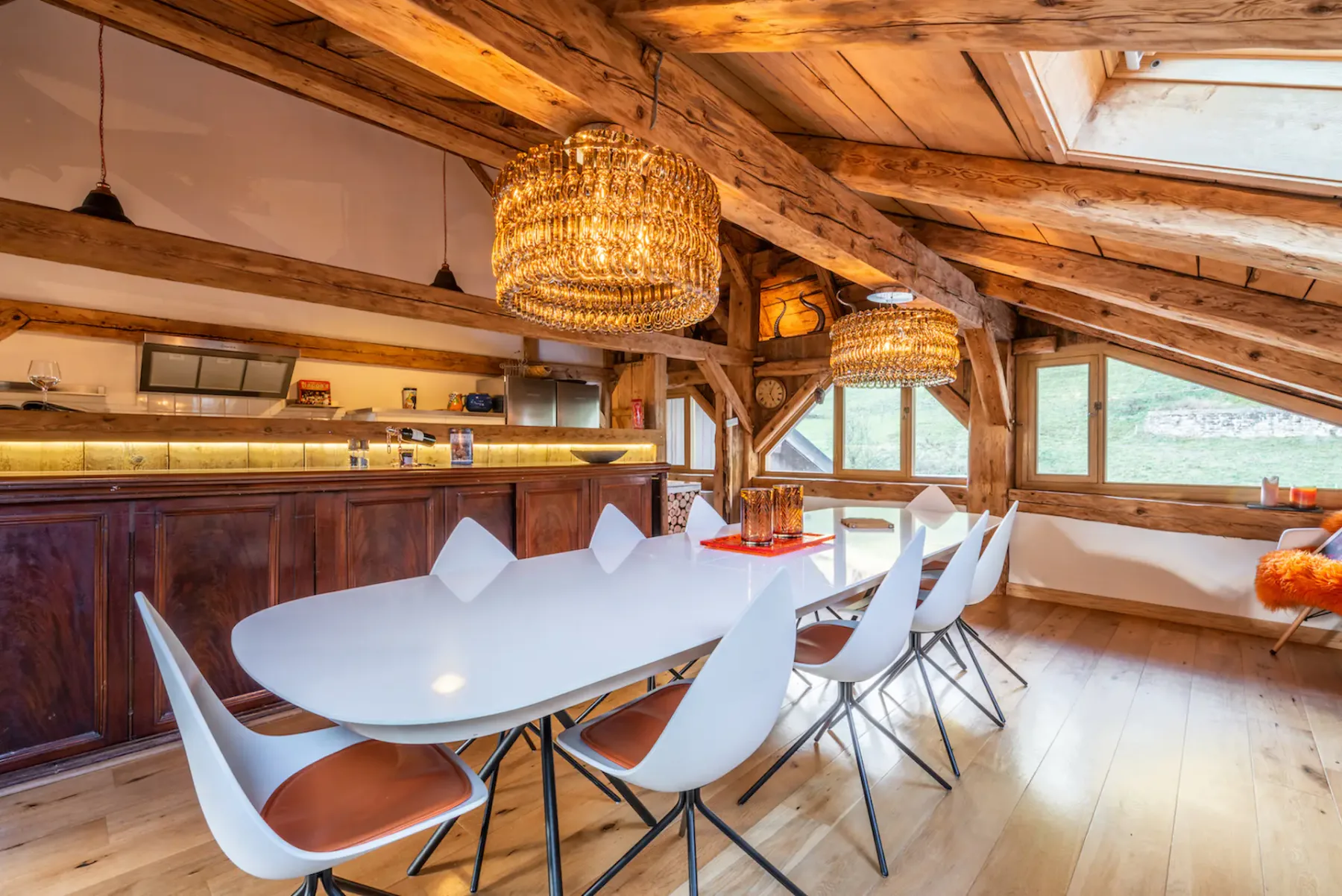 A dining area with a long table and white chairs beneath exposed wooden beams.