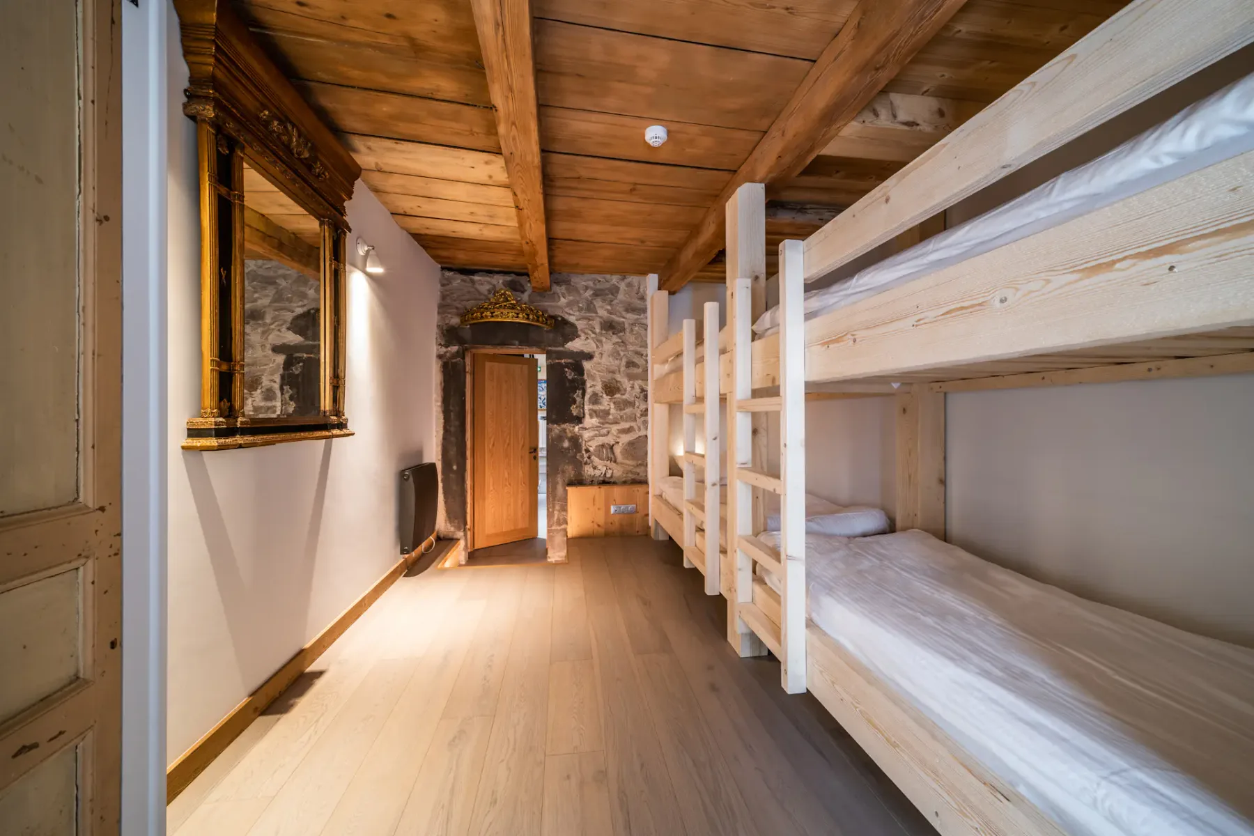 A rustic bedroom with wooden bunk beds and a stone wall.