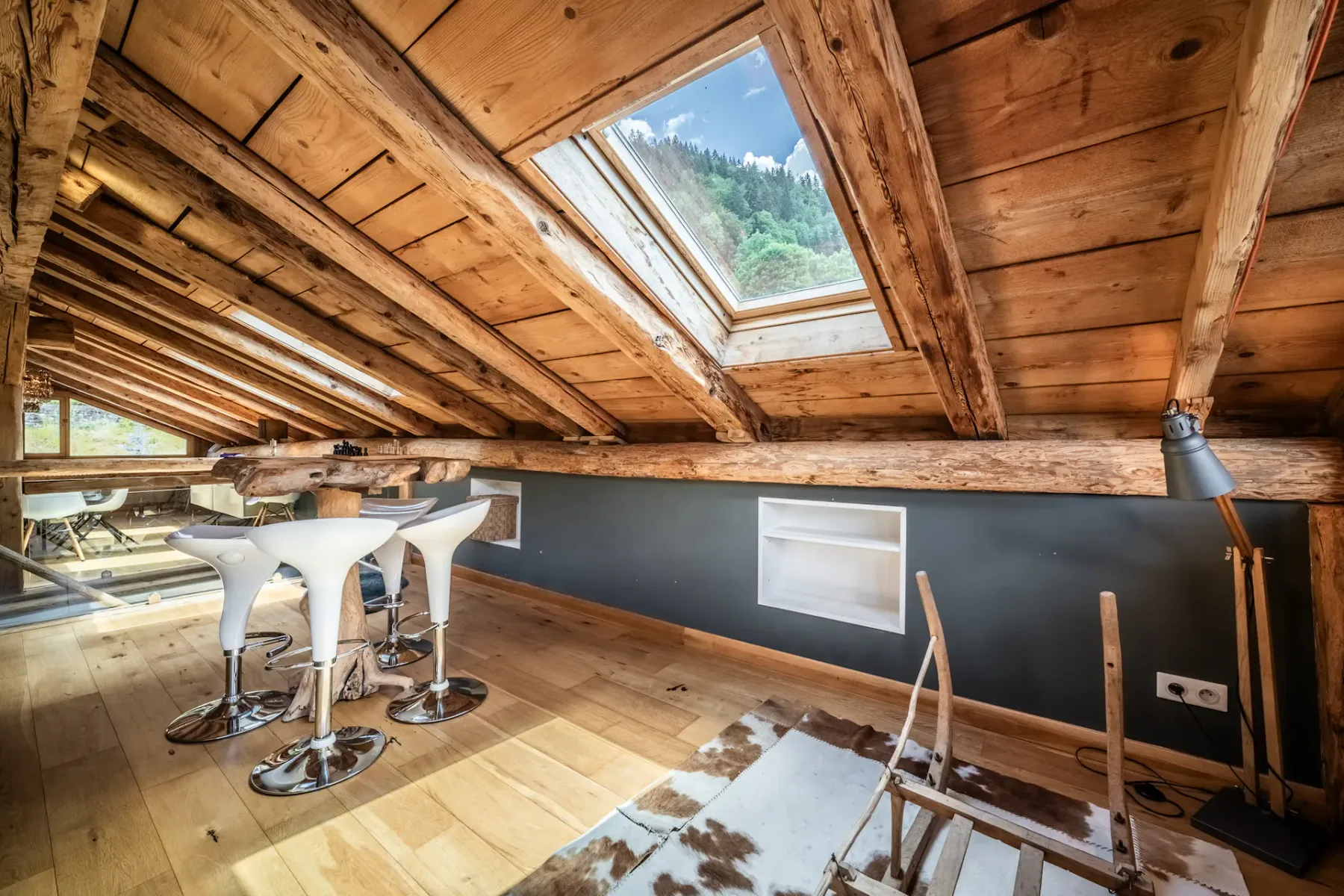 A wood-paneled attic room has a skylight, bar seating, and a desk.