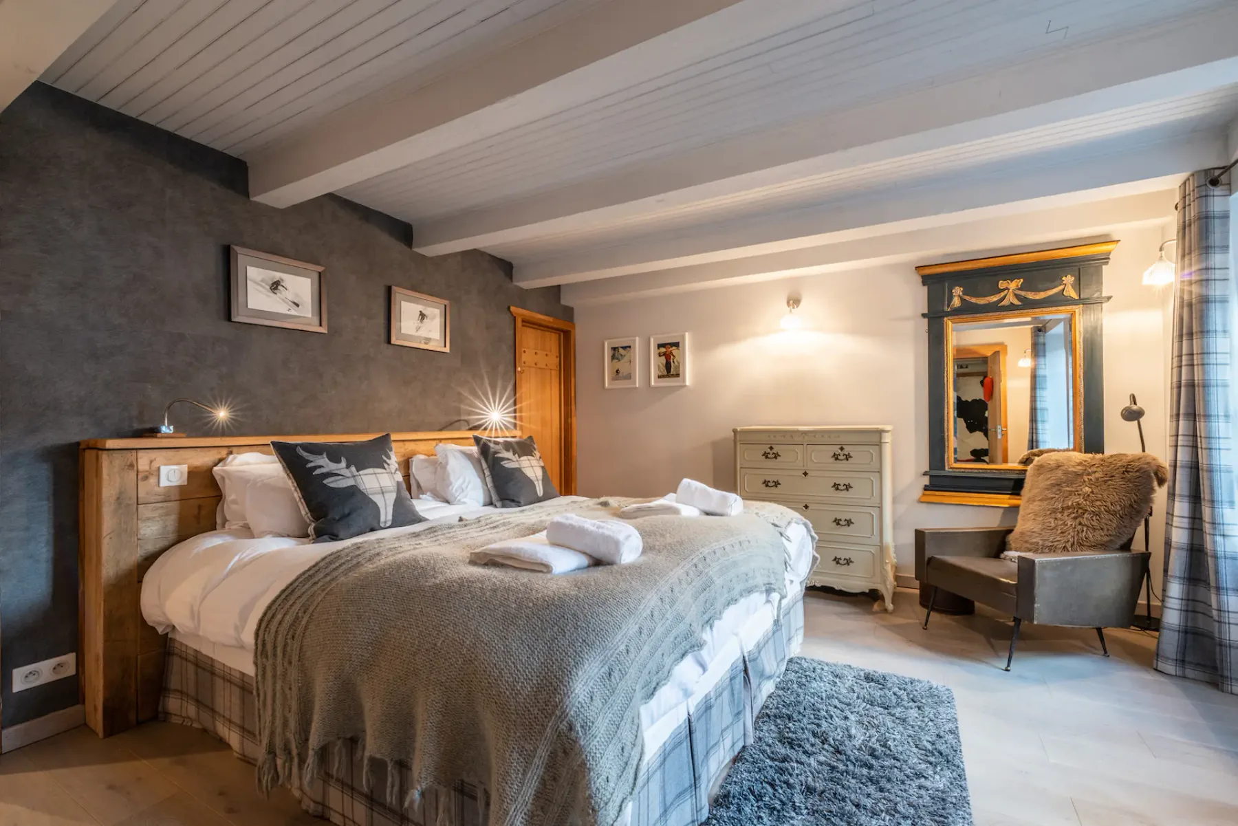 A bedroom with a large bed, bedside lights, and a chair beside a mirror.