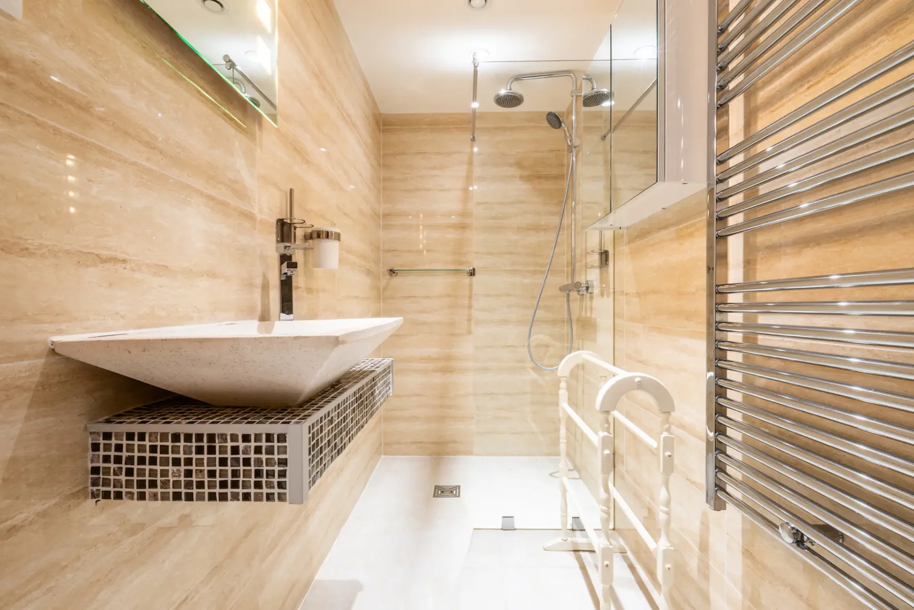 A tiled bathroom features a wall-mounted sink and a glass-enclosed shower.