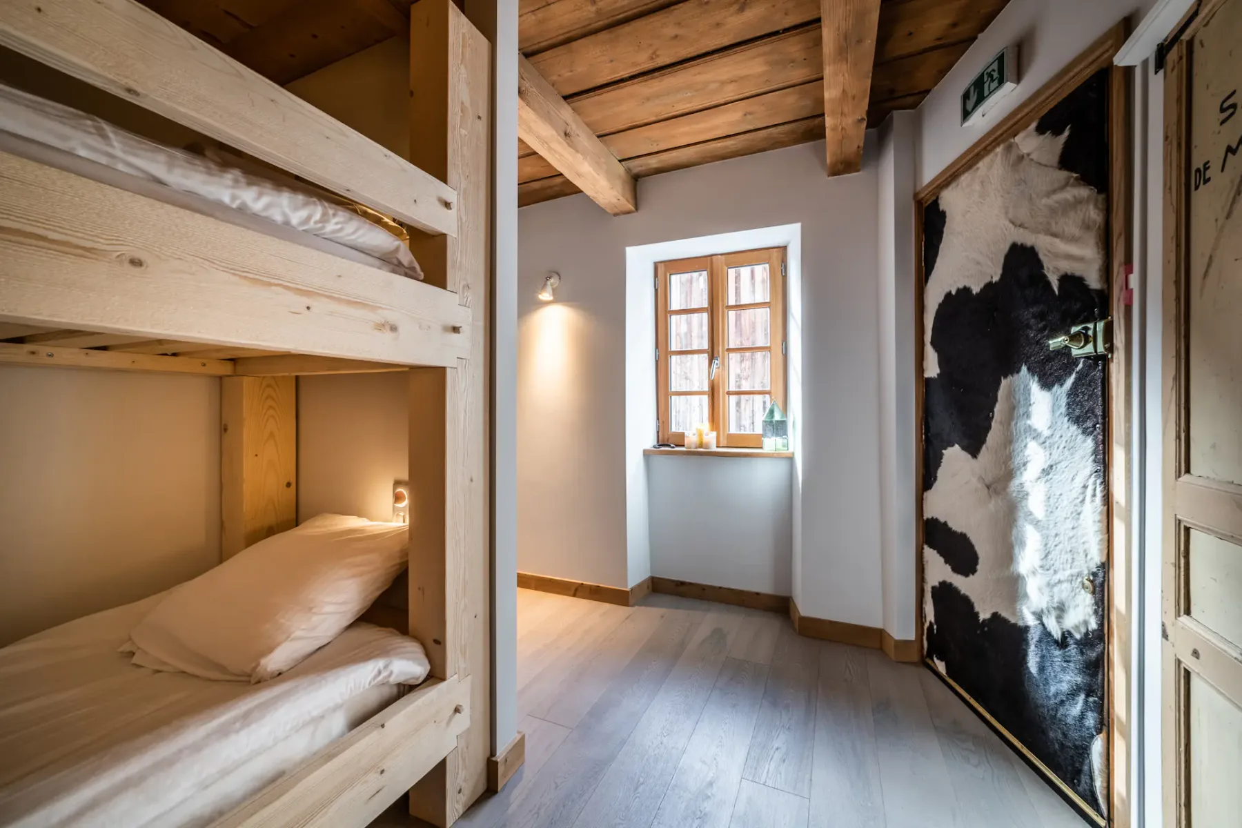A bedroom with wooden bunk beds, a window, and a cow-patterned door.