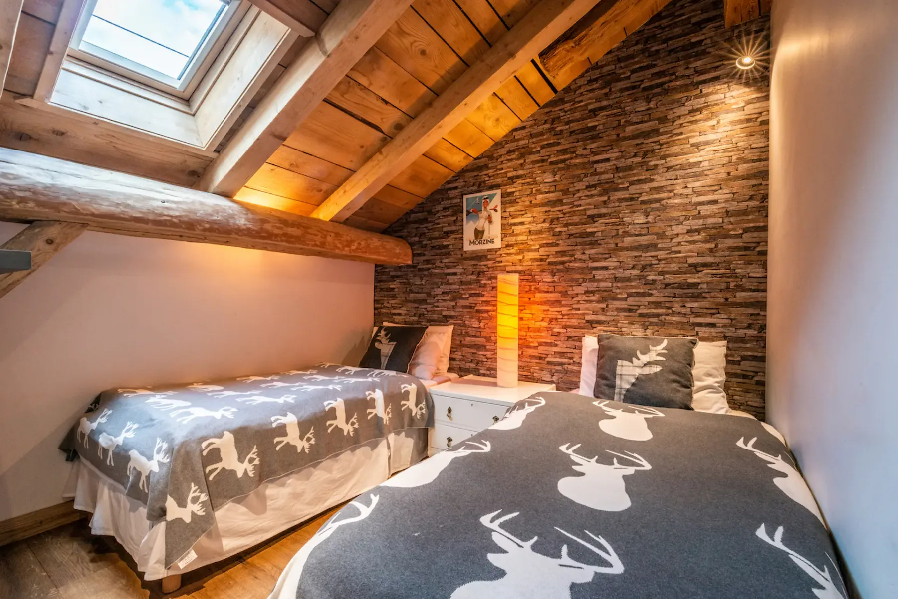 A bedroom with two single beds beneath a sloped wooden ceiling and skylight.