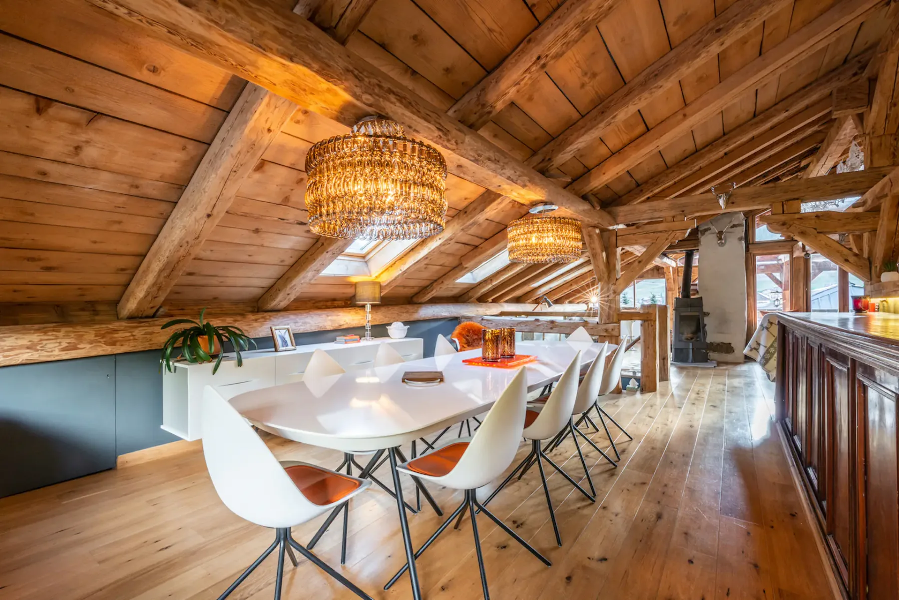 A dining area with a long table and chairs beneath a sloped wooden ceiling.