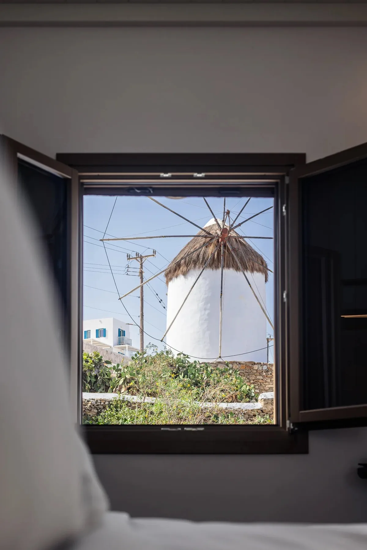 A bedroom window opens onto a view of a white windmill and greenery.