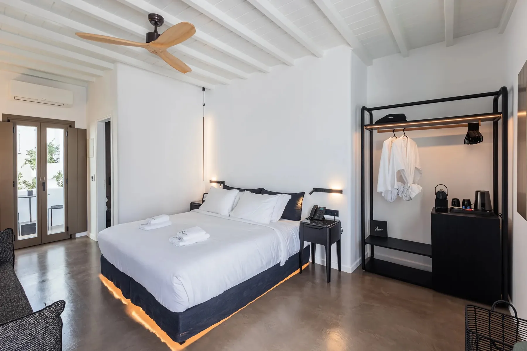 Dormitorio con una cama arreglada y un perchero abierto.